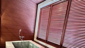 Un baño moderno con una bañera rectangular grande, paneles de madera y una ventana con persianas horizontales.