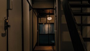 A narrow hallway with wooden flooring, a staircase on the right, and a door on the left. - Machiya Villa Gashu (Nagoya)