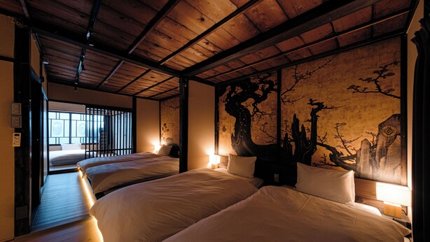 A hotel room with three beds, wooden flooring, and a large wall painting. - Machiya Villa Gashu (Nagoya)