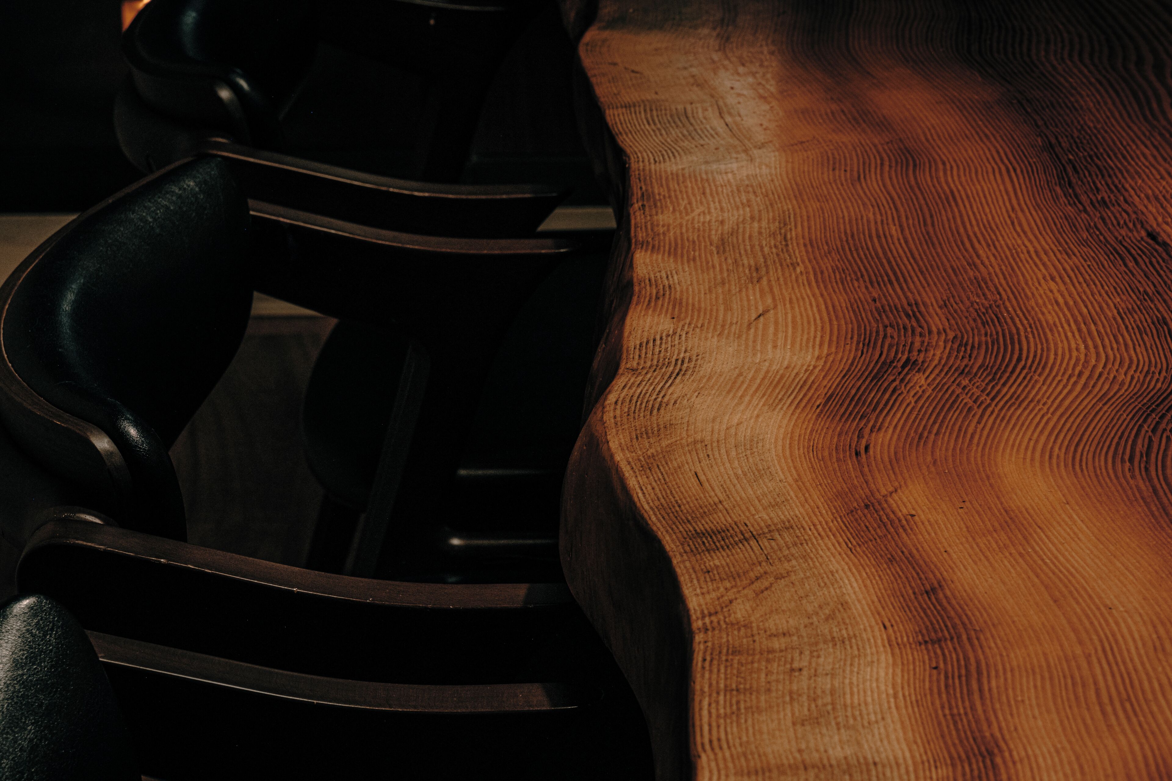 A close-up of a wooden table with a visible grain pattern and a black chair with a curved backrest.