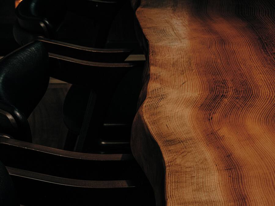 A close-up of a wooden table with a visible grain pattern and a black chair with a curved backrest.