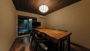 A dining area with a wooden table and chairs, a ceiling light fixture, and a view through a glass door.