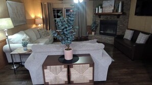 Una sala de estar acogedora con chimenea, un sofá, una mesa de centro con un florero y una lámpara.