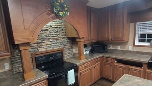 Una cocina con armarios de madera, una pared de acento de piedra, una estufa negra y un microondas.
