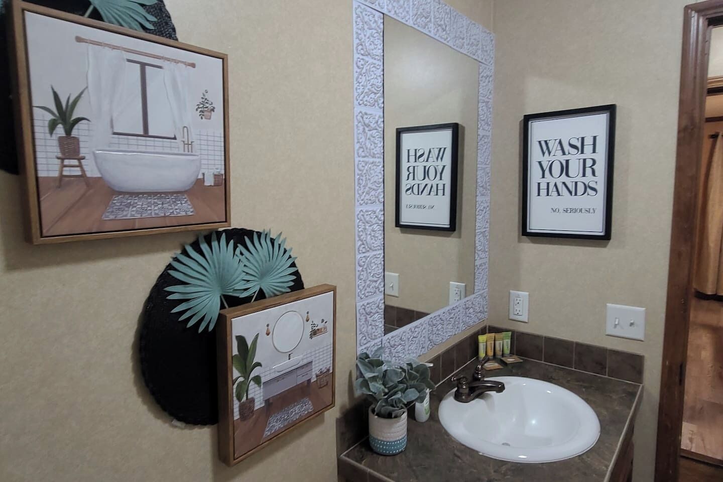 A bathroom with a large mirror, a sink, and framed artwork on the walls.