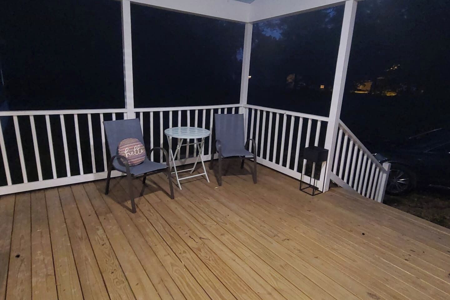 A covered outdoor area with a wooden deck, two chairs, a small round table, and a white railing.