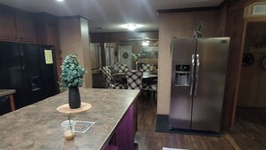 Una cocina con encimera de granito, refrigerador de acero inoxidable y comedor con mantel a cuadros.