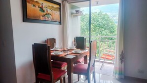A dining area with a table set for four, chairs, a painting on the wall, and a balcony with a view. - Very natural, Peaceful and Centrally in Medellín (Envigado)