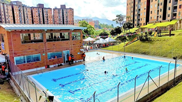 A swimming pool surrounded by a brick building with multiple windows, a grassy area, and a playground. - Very natural, Peaceful and Centrally in Medellín (Envigado)