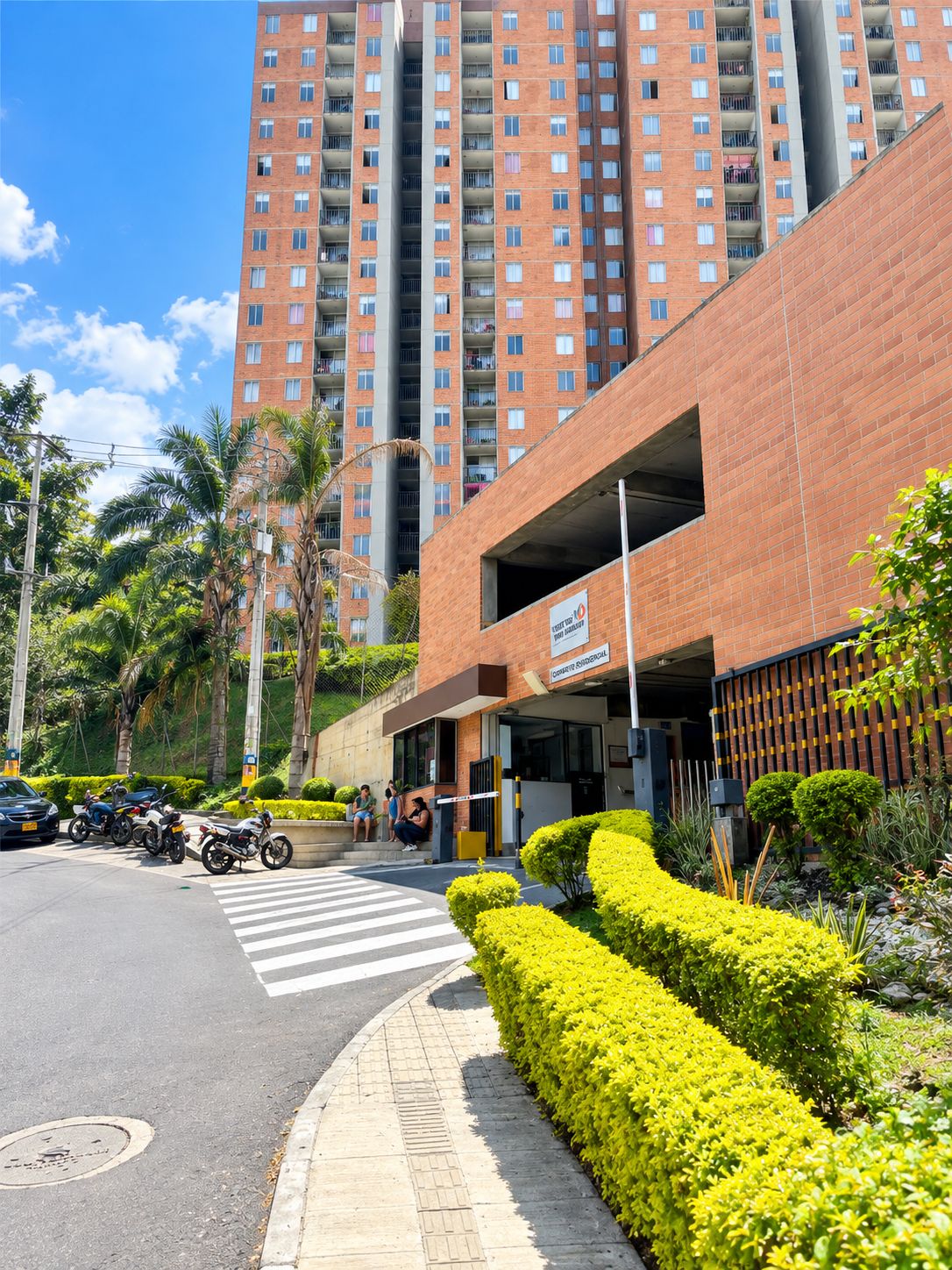 Edifício com vários andares e entrada para garagem, cercado por vegetação e palmeiras.