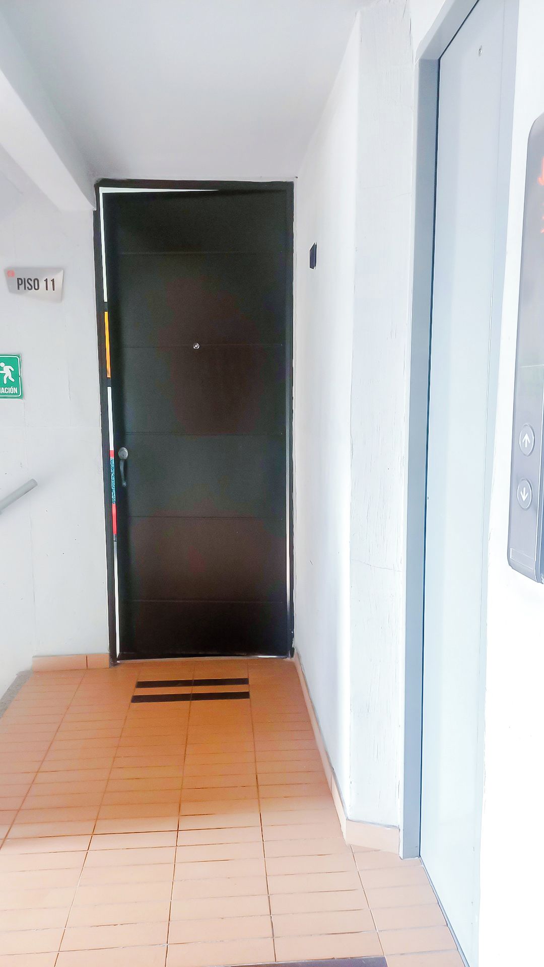 Un pasillo con una puerta cerrada, un letrero que indica 'PISO 11' y una señal de salida de emergencia.