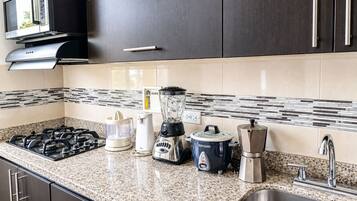 Una cocina con estufa a gas, microondas, licuadora, cafetera y un lavabo.