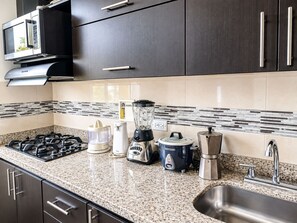 Una cocina con estufa a gas, microondas, licuadora, cafetera y un lavabo.