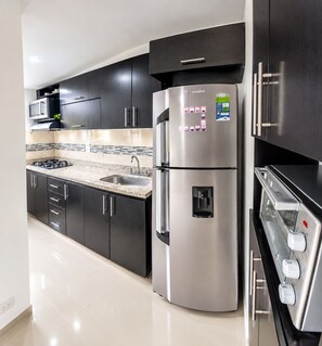 A modern kitchen with dark cabinets, a stainless steel refrigerator, a built-in oven, and a microwave.