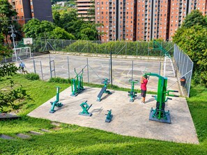 Zona de gimnasio al aire libre con equipo de ejercicio y una cancha de baloncesto.