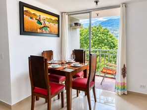 A dining area with a table set for four, red cushioned chairs, and a large window with a view of greenery and mountains.