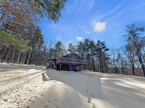 Eine Holzhütte mit einer Holzterrasse und einer überdachten Veranda, umgeben von verschneitem Gelände und Bäumen.