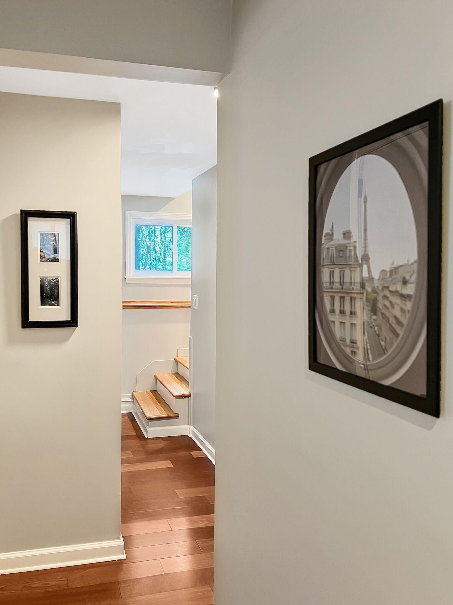 A hallway with framed artwork, wooden flooring, and a staircase leading to an upper level.