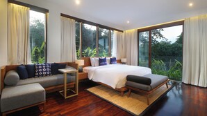Ein modernes Schlafzimmer mit einem großen Bett, einer Couch und einem kleinen Tisch. Große Fenster mit Vorhängen und Holzböden.