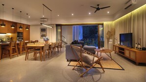 Ein modernes Wohnzimmer mit Essbereich, einer Couch, einem Fernseher und einem Balkon mit Blick auf Gebäude.