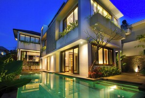 Una casa moderna de dos pisos con piscina, ventanas amplias y mobiliario de exterior.