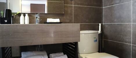 A modern bathroom with a toilet, sink, and mirror. There are towels and toiletries on the counter.