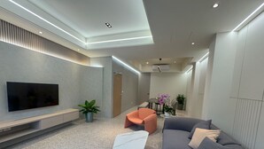 A modern living room with a flat-screen TV, a marble coffee table, a grey sofa, and a small orange chair. - Longtan Lake Inn (Jiaoxi)