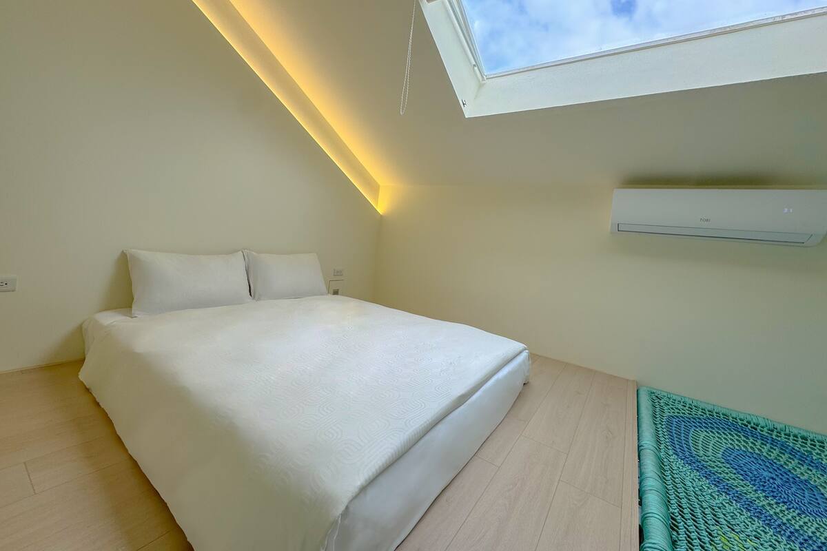 Ein Schlafzimmer mit Oberlicht, einem Bett, einer Klimaanlage und einem gemusterten Teppich.