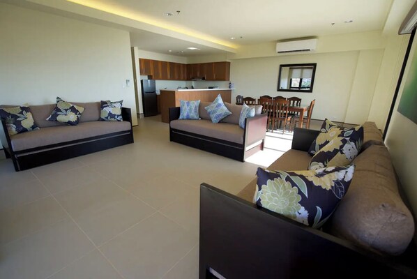 A modern living room with two sofas, a dining area with chairs, and a kitchen in the background.