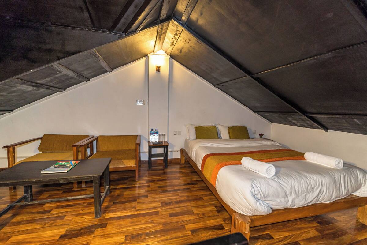 A cozy attic bedroom with a wooden floor, a bed with white bedding, a small table, and a chair.