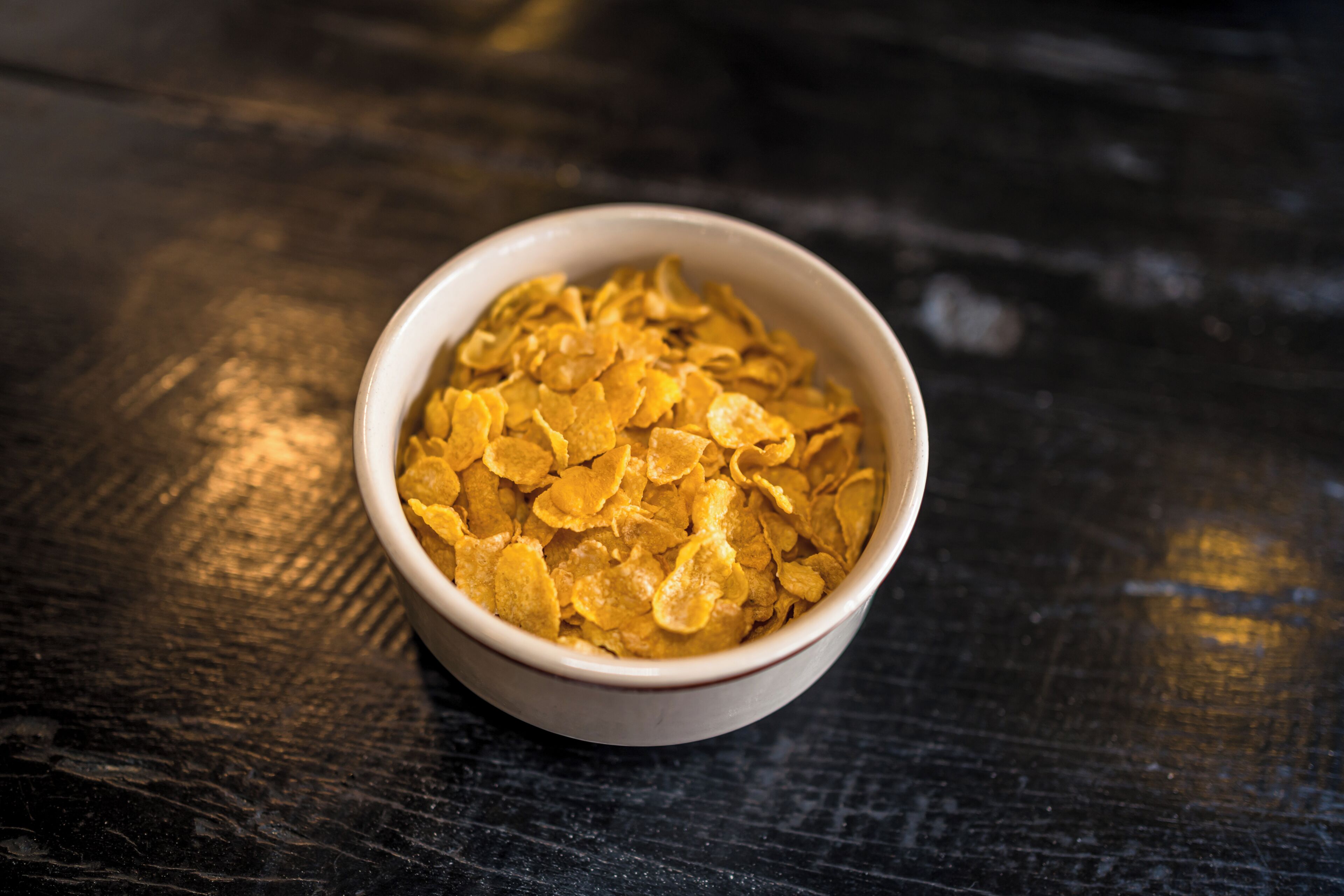 A bowl of cornflakes on a dark wooden surface.