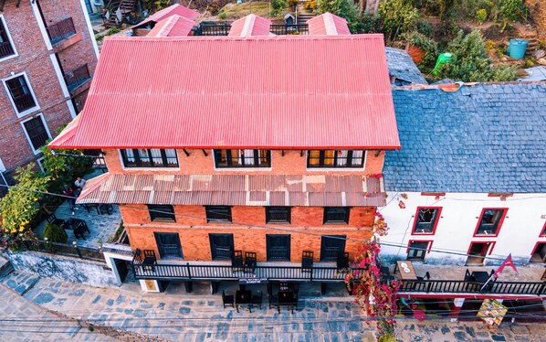 A multi-story building with a red roof, a balcony with seating, and a sign indicating it is a hotel.