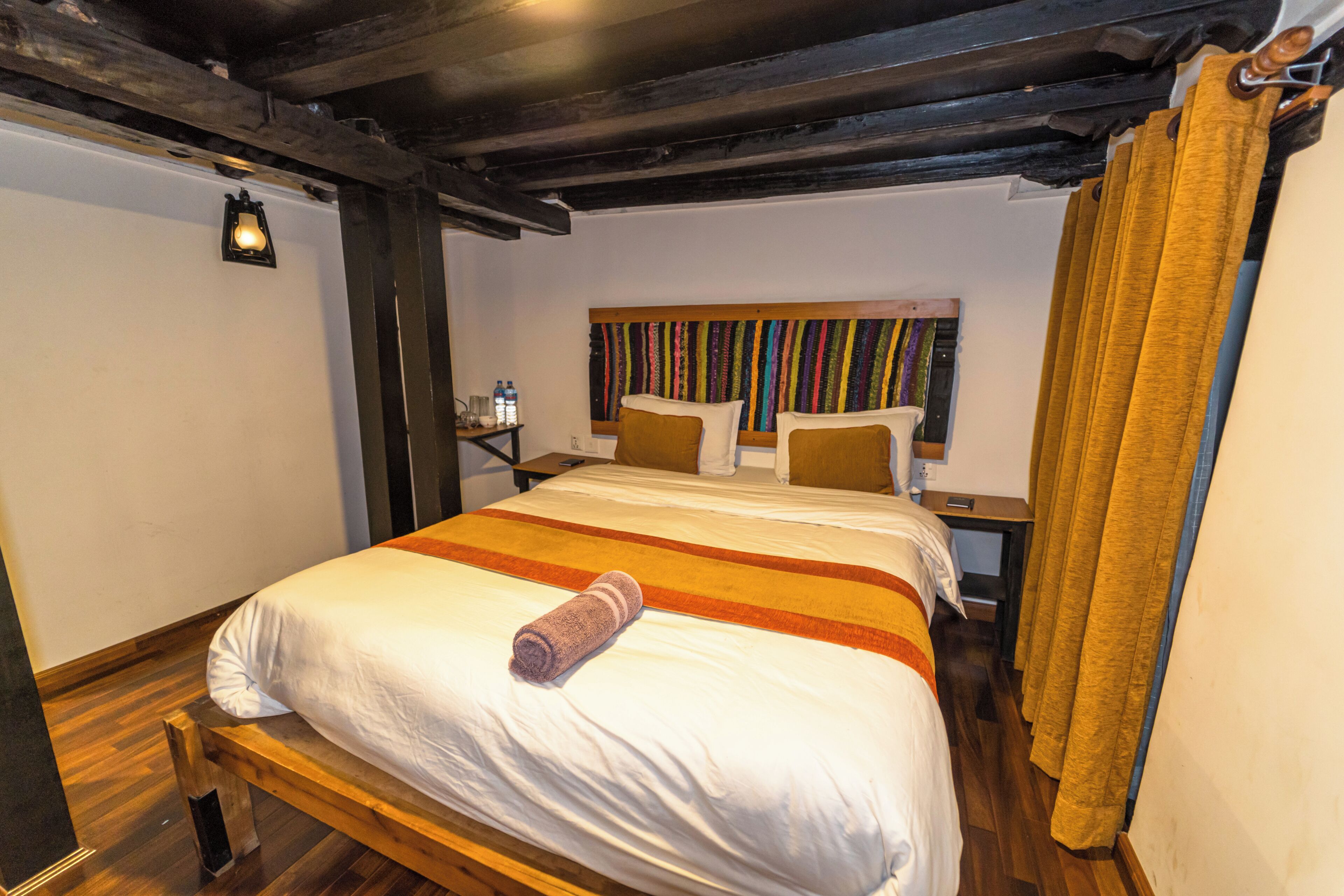 A neatly made bed with a rolled towel, a wooden headboard, and a colorful striped headboard.