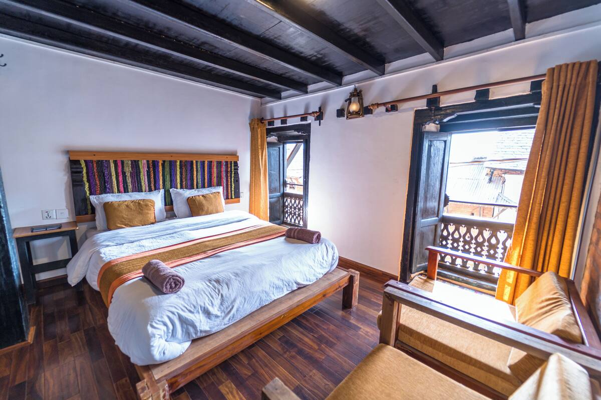 A bedroom with a wooden bed, a nightstand, a chair, and a window with curtains.