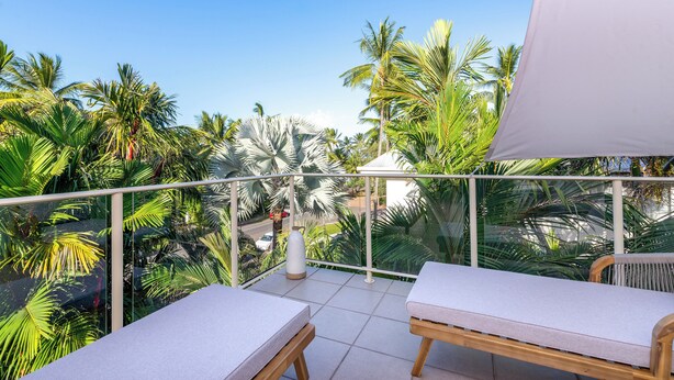A balcony with two sunbeds, a glass railing, and a view of palm trees. - Driftwood Mantaray Two Bedroom Two Bathroom Penthouse (Port Douglas)