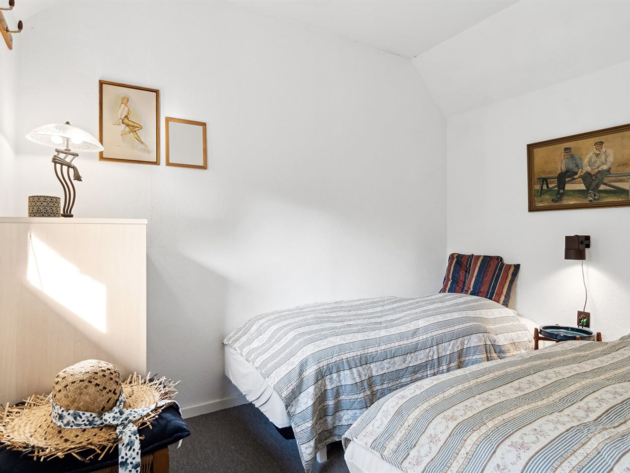 A bedroom with two beds, a desk, a lamp, and wall art.