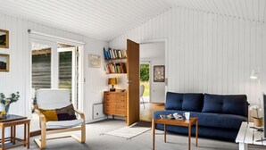 Un salon moderne avec un canapé bleu, une table d’appoint en bois, un fauteuil blanc et une bibliothèque.
