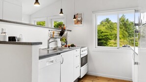 Une cuisine moderne avec des meubles blancs, un évier en acier inoxydable, un lave-vaisselle Bosch et une fenêtre donnant sur un paysage verdoyant.