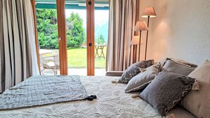A bedroom with a bed, pillows, a floor lamp, and a view of a garden through a sliding door. - Baudrier A05 by Interhome (Verbier)