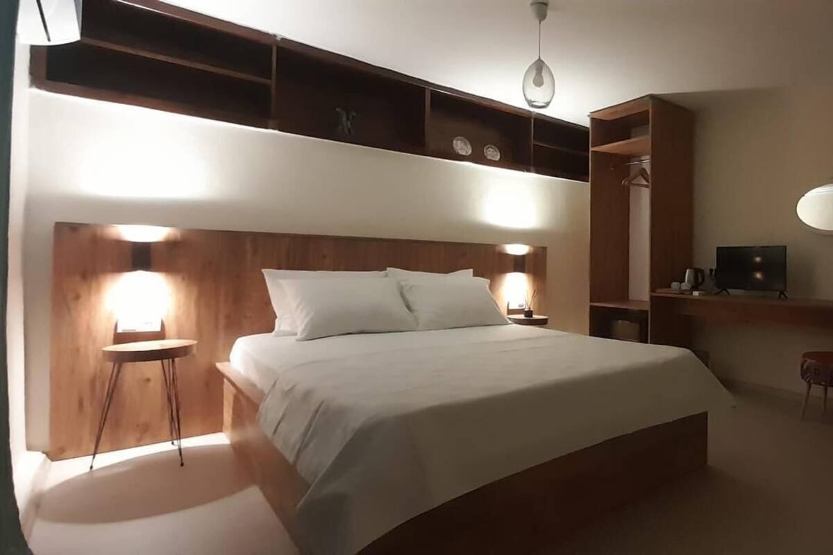 A bedroom with a large bed, bedside tables, a wardrobe, a mirror, and a small stool.