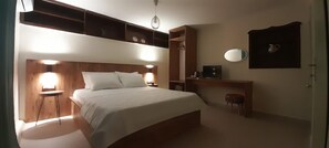 A bedroom with a large bed, bedside tables, a wardrobe, a mirror, and a small stool.
