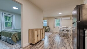 Una habitación amplia con cama, un aparador de madera, un rincón comedor con mesa y sillas, y un refrigerador negro.