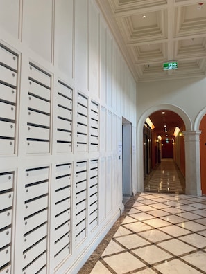 A hotel corridor with lockers, a tiled floor, and an arched doorway.