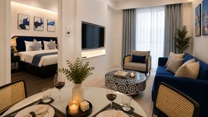 Ein modernes Hotelzimmer mit Bett, einer Couch, einer Essecke mit Tisch für zwei Personen und einem an der Wand montierten Fernseher.