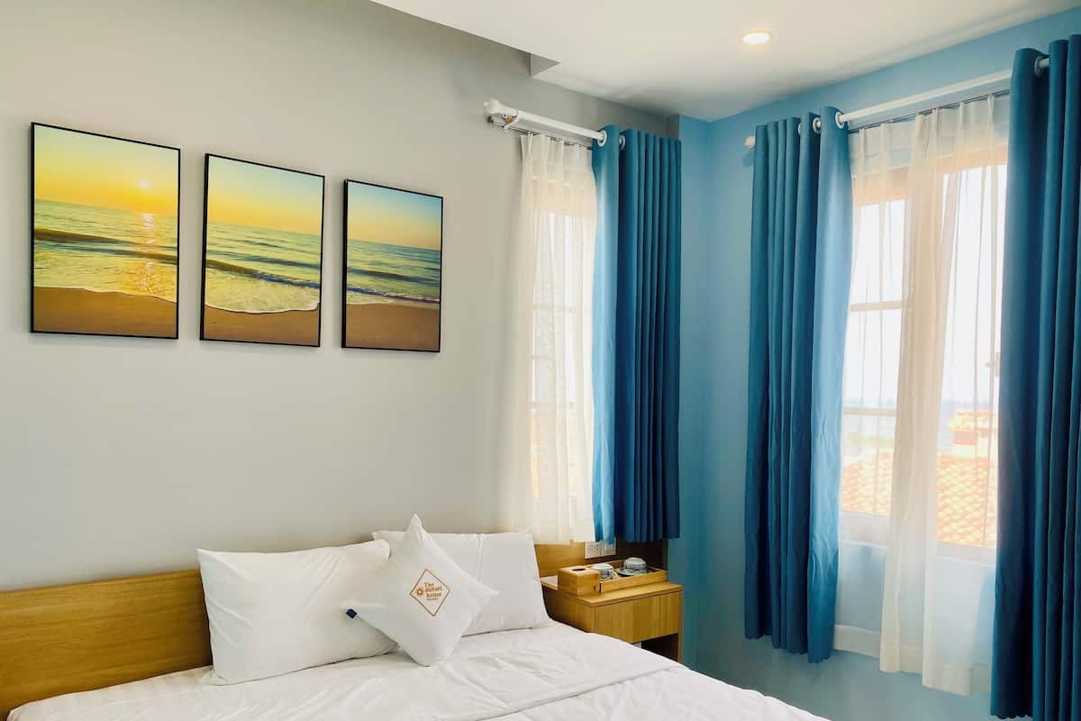 A hotel room with a bed, white bedding, a wooden headboard, a nightstand with a lamp, and three framed pictures on the wall.