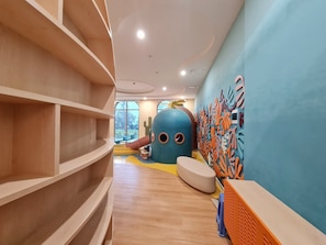 A children's play area with a large blue octopus decoration, wooden shelves, and a colorful wall mural.