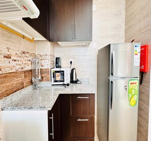 A compact kitchen with dark wooden cabinets, a built-in microwave, a kettle, and a stainless steel refrigerator. - OYO 1186 Home Orion BLDG Arjan 1 BHK (Dubai)