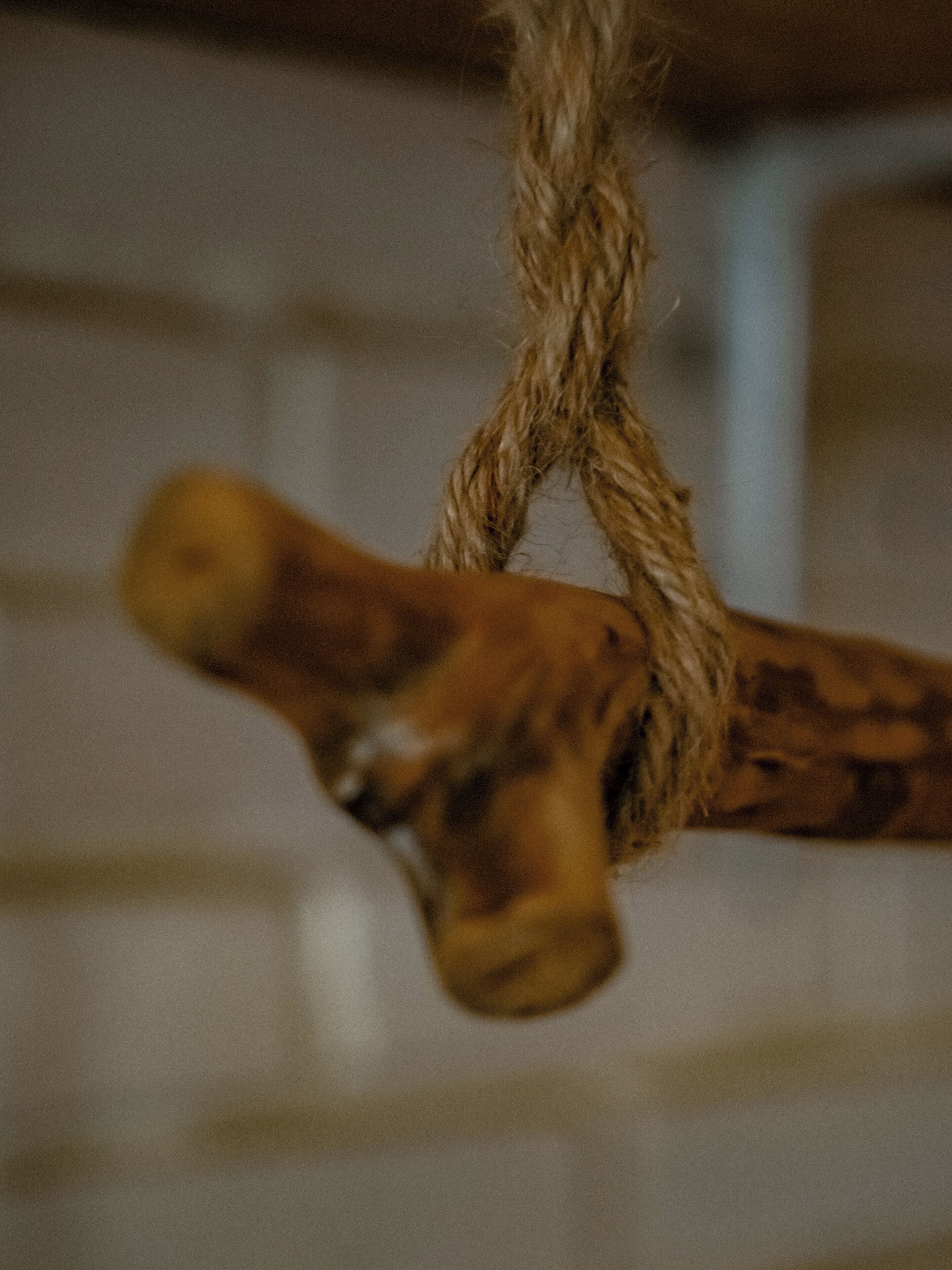 A close-up of a rope tied around a wooden object, possibly a part of a piece of furniture or decor.