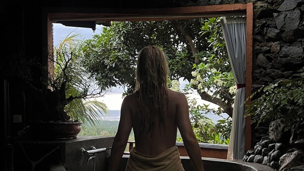 A person in a stone bathtub with a view of lush greenery and a stone wall. - Kailash Lodge  (Tejakula)