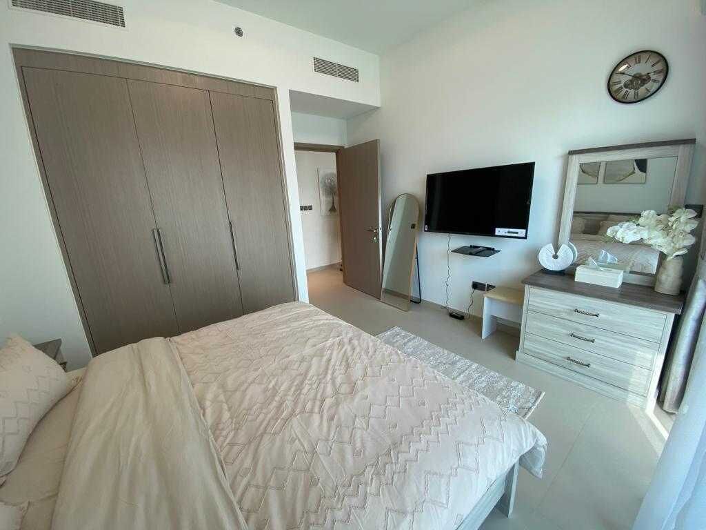A bedroom with a bed, a wardrobe, a television, a mirror, and a clock on the wall.